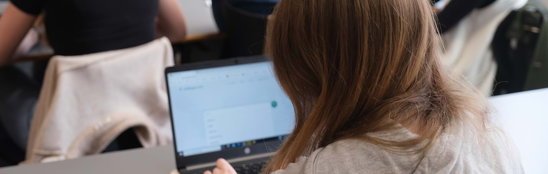 Pige set bagfra laver skriftlig opgave på bærbar computer