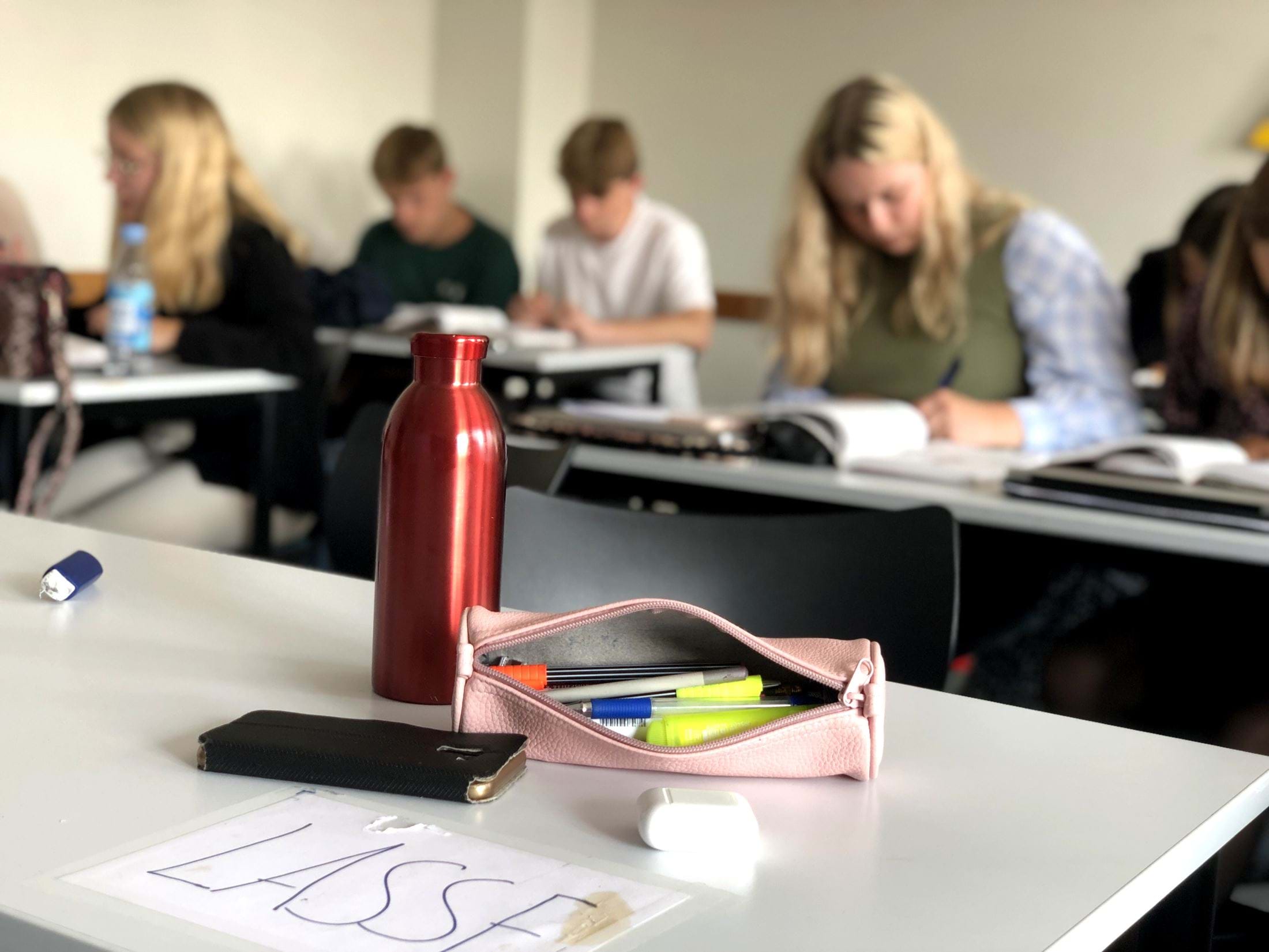 En tom plads ved et skrivebord med elever i baggrunden