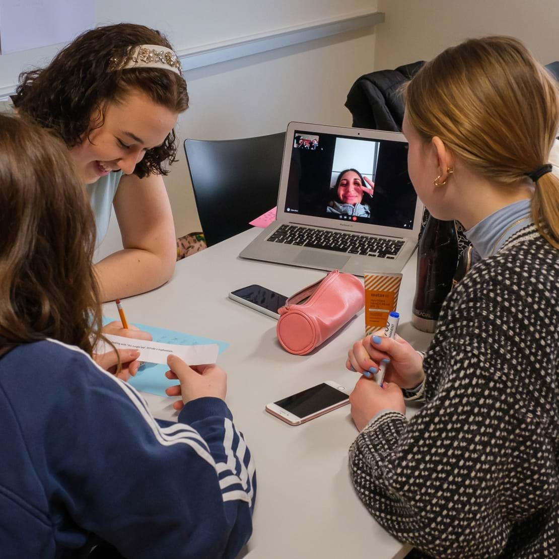 Tre elever laver gruppearbejde mens en fjerde elev er med virtuelt på tændt bærbar computer