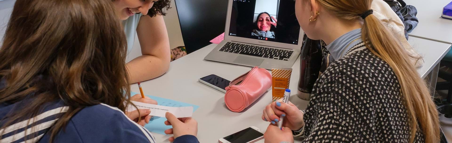 Tre elever laver gruppearbejde mens en fjerde elev er med virtuelt på tændt bærbar computer
