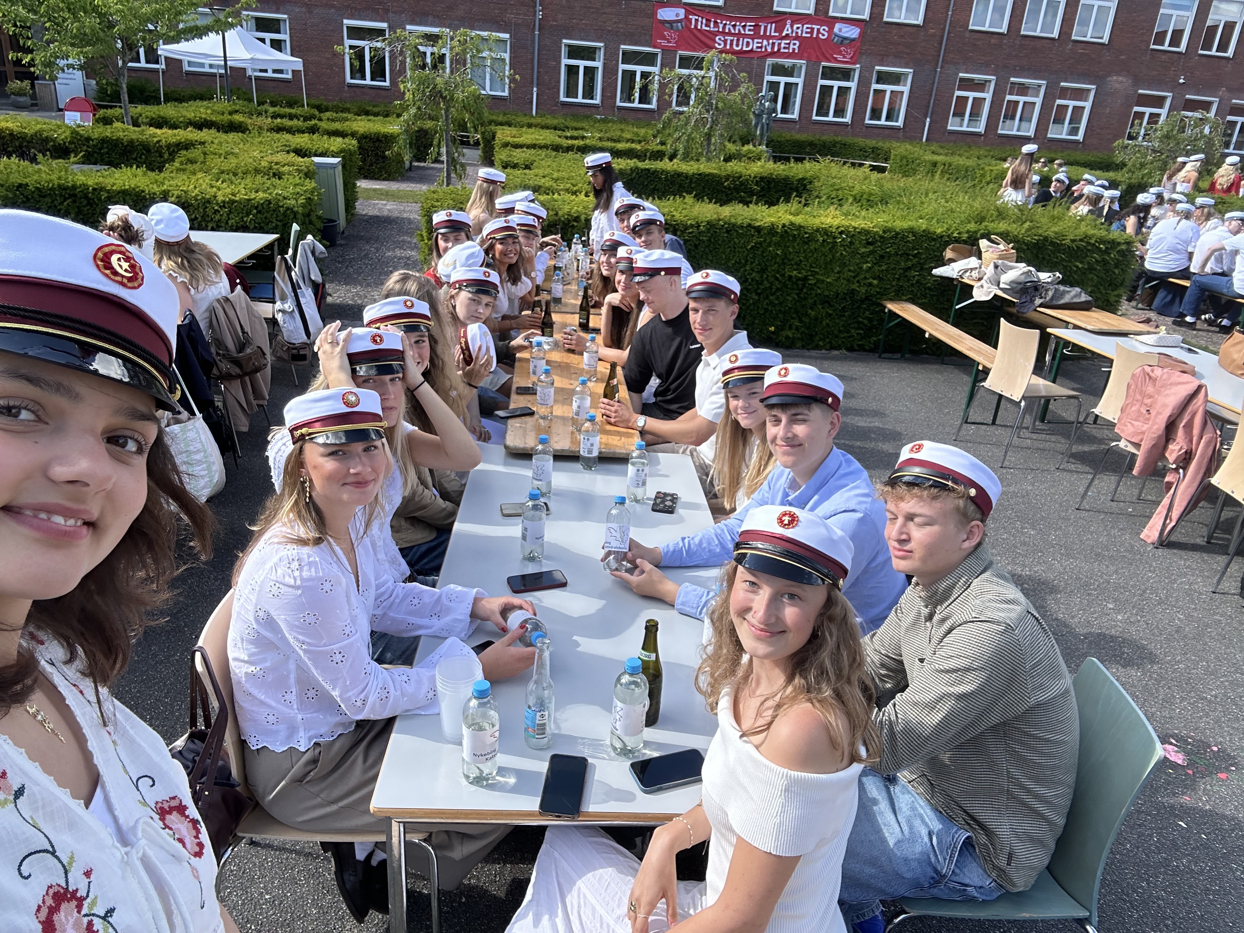 Glade studenter ved stort fælles bord i skolegården