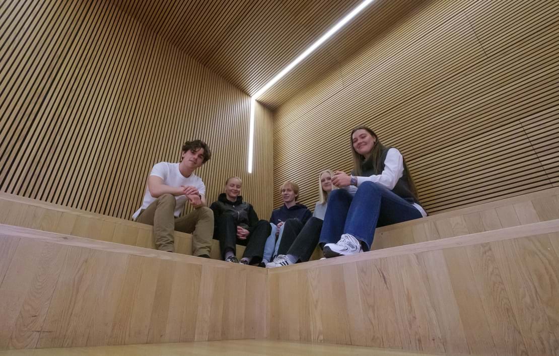 Fem elever sidder på indendørs trætrappe