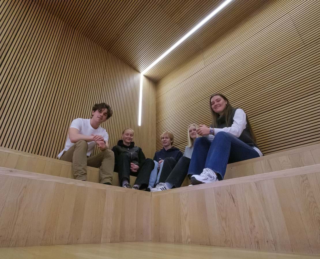 Fem elever sidder på indendørs trætrappe