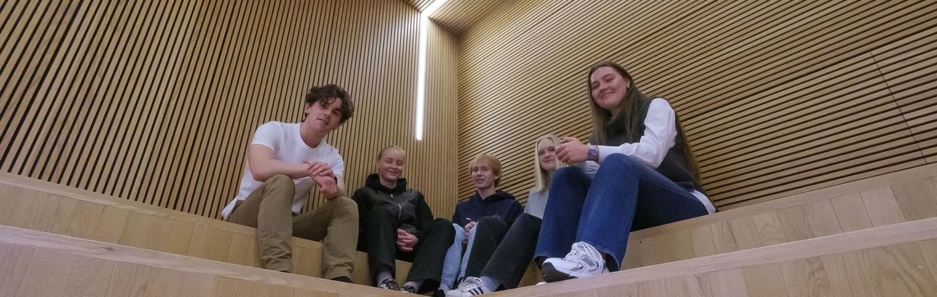 Fem elever sidder på indendørs trætrappe