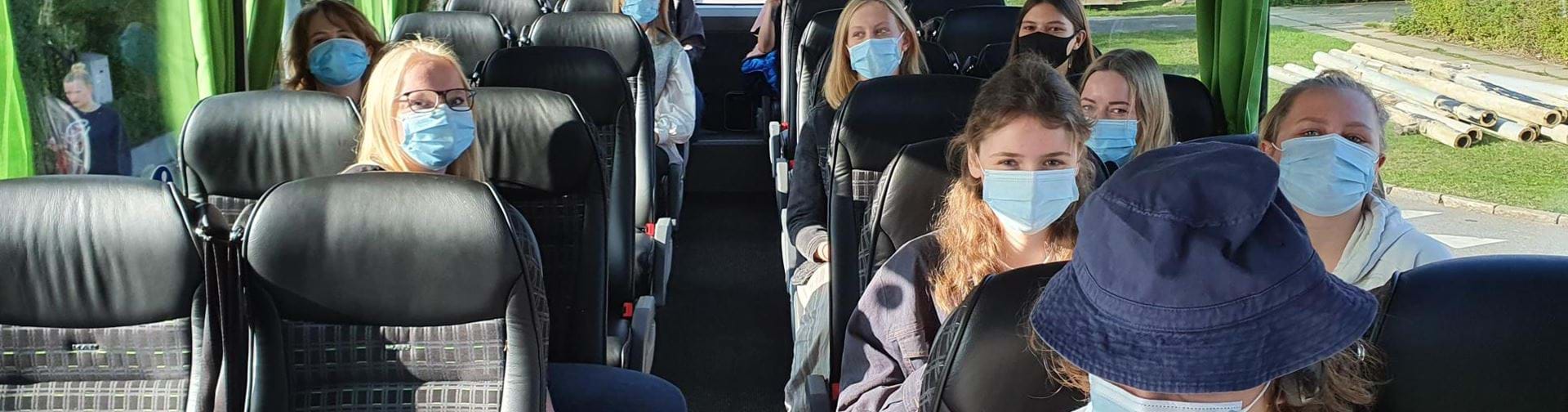 Elever med mundbind på i en bus på vej på tur