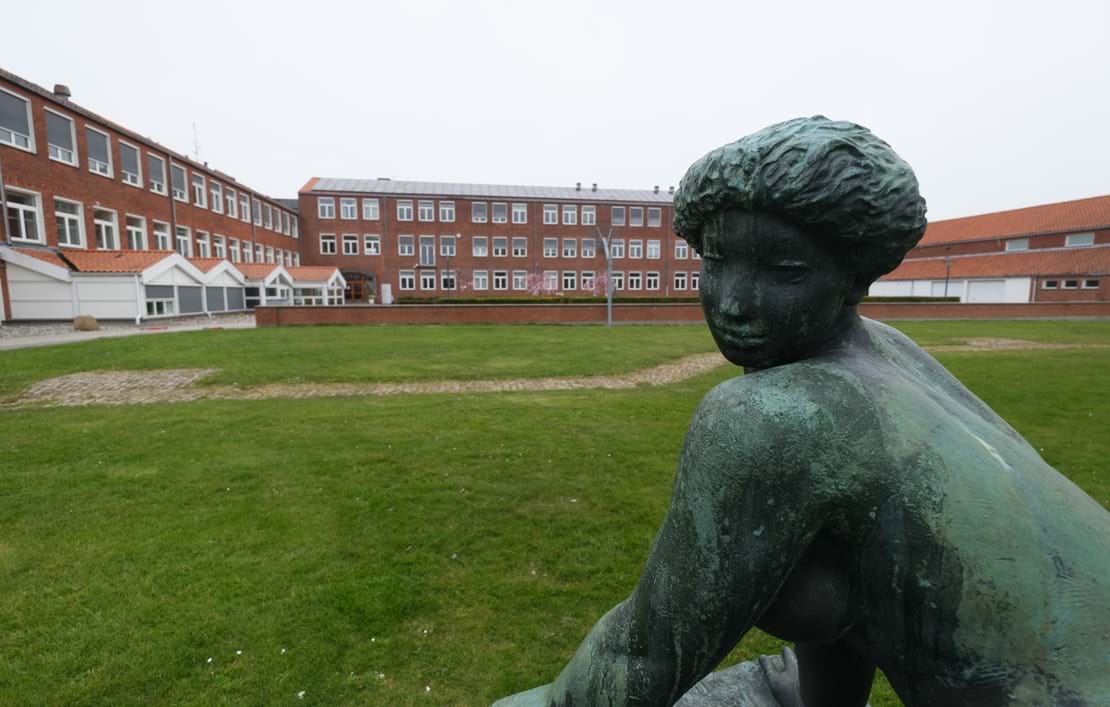 Nykøbing Katedralskoles bygninger set udefra med en statue i forgrunden