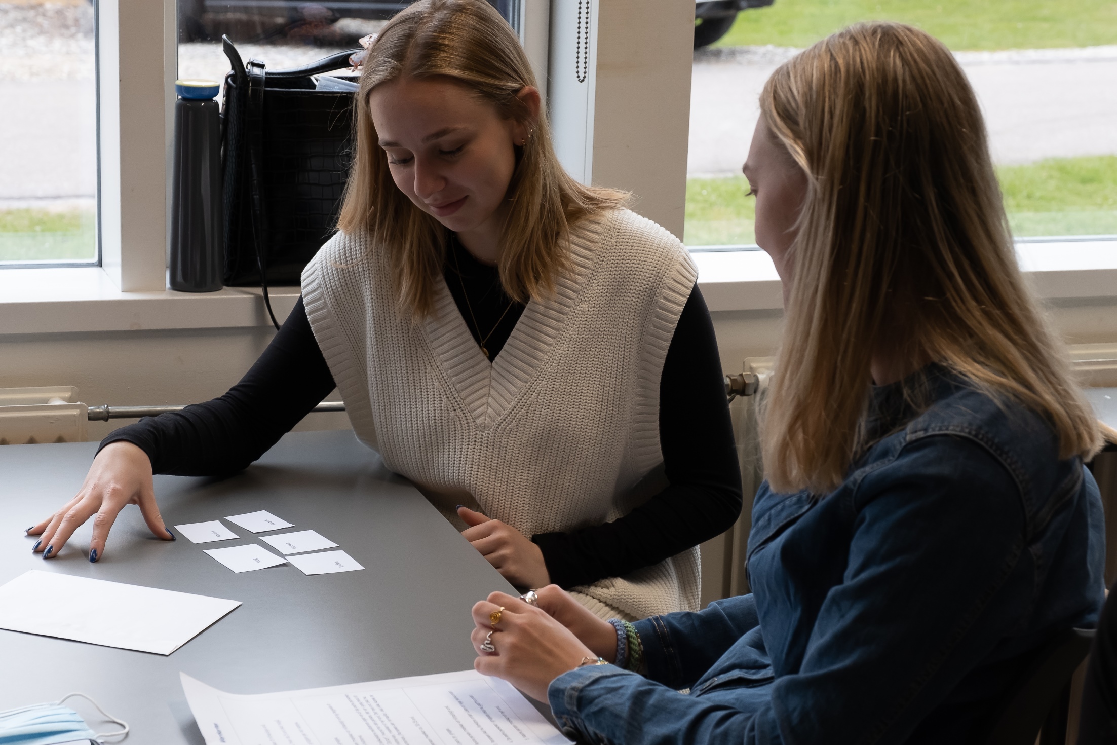 To piger sidder ved bord og kigger på små hvide sedler