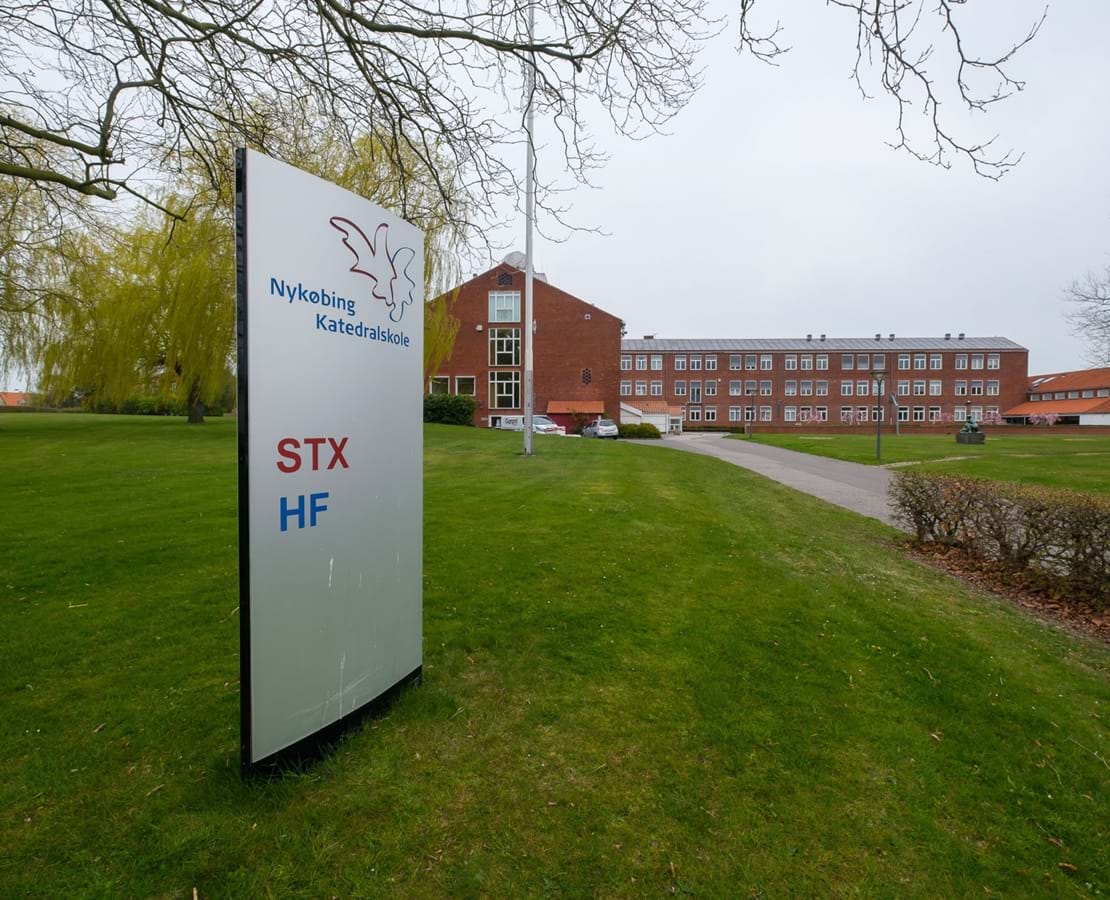Skilt hvorpå der står Nykøbing Katedralskole STX og HF. I baggrunden skolens bygninger.