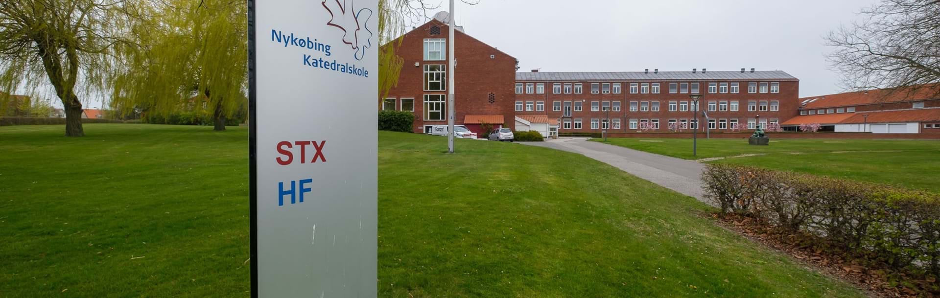 Skilt hvorpå der står Nykøbing Katedralskole STX og HF. I baggrunden skolens bygninger.