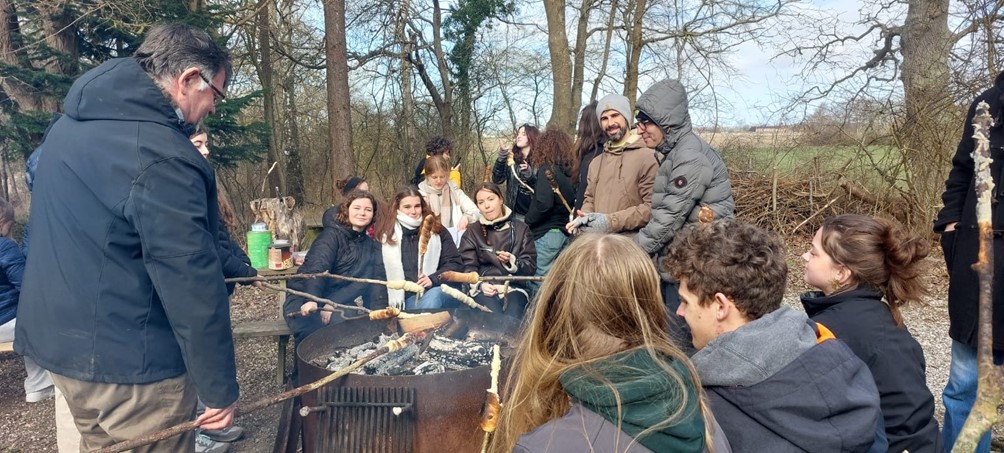 Elever og lærere omkring en olietønde med gløder, hvor de laver snobrød på pinde